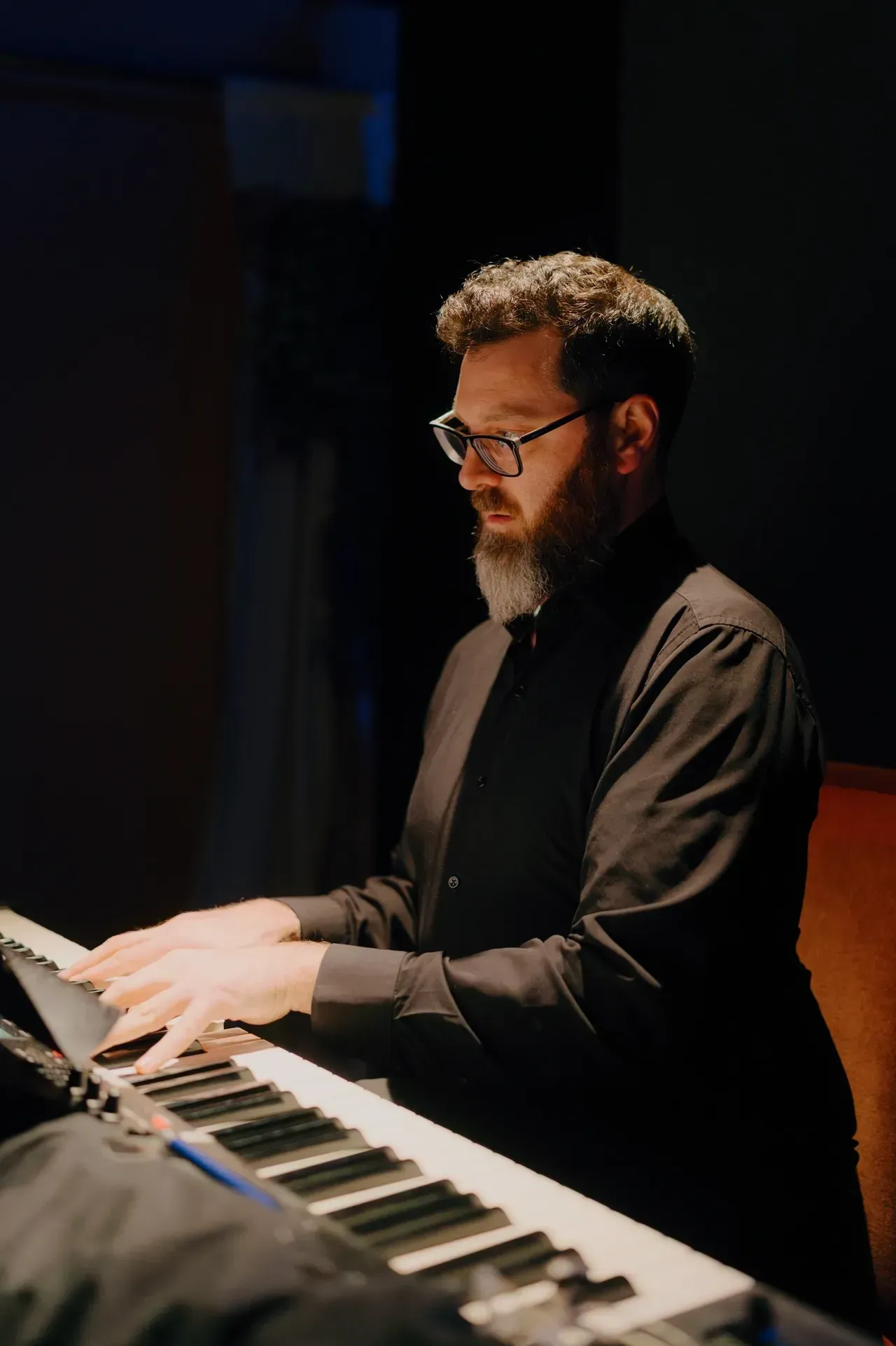 Man playing keyboard on a dimly lit stage, focused under warm spotlights