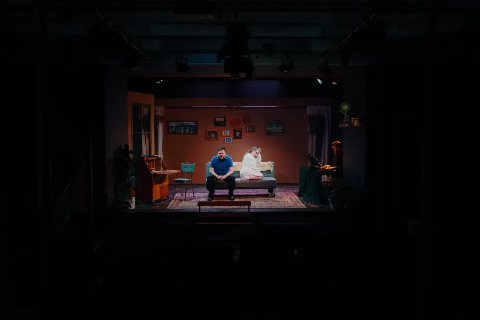 Two people on a couch in a dim, cozy living room set with warm lighting and a rug.