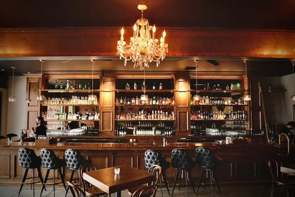 Elegant bar interior with chandelier, backlit shelves, and tufted stools along a polished wooden counter