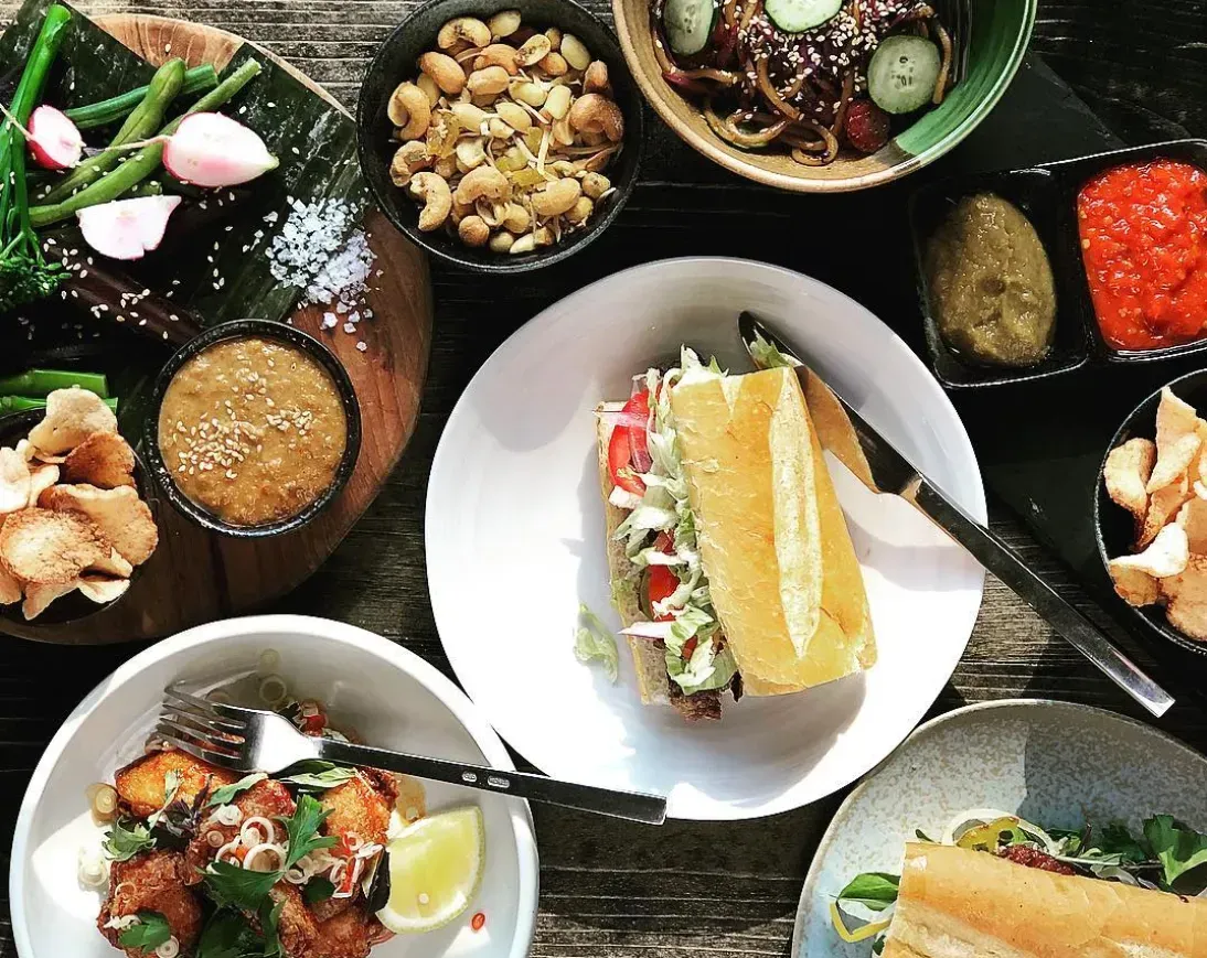 Assorted Vietnamese dishes on a rustic table, including sandwiches, bowls, and dipping sauces.