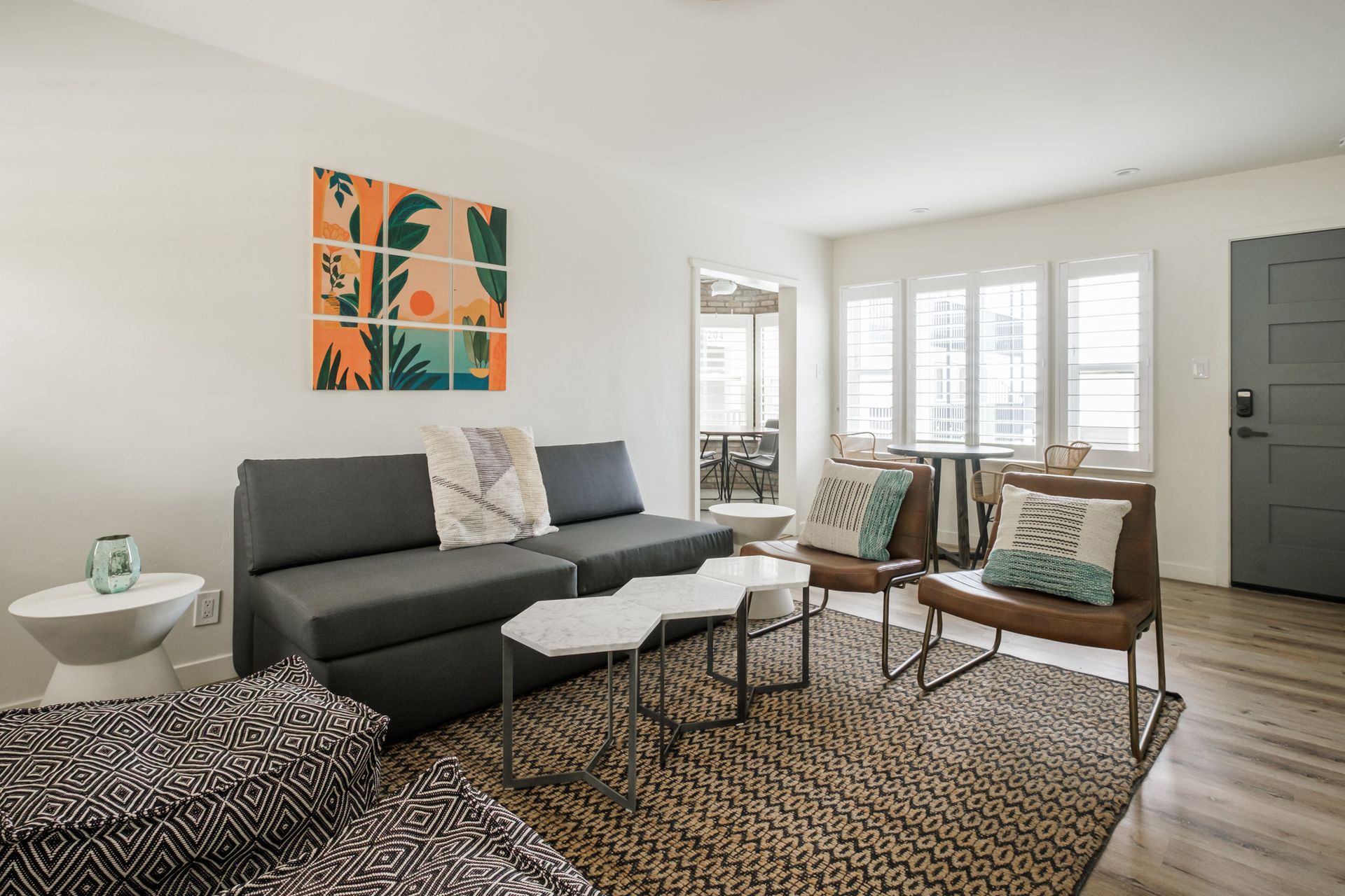 Modern living room with gray sofa, two chairs, coffee table, woven rug, and bright windows