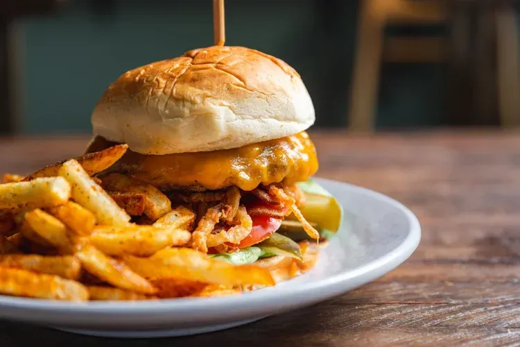 Burger with melted cheese and fries on a white plate on a wooden table