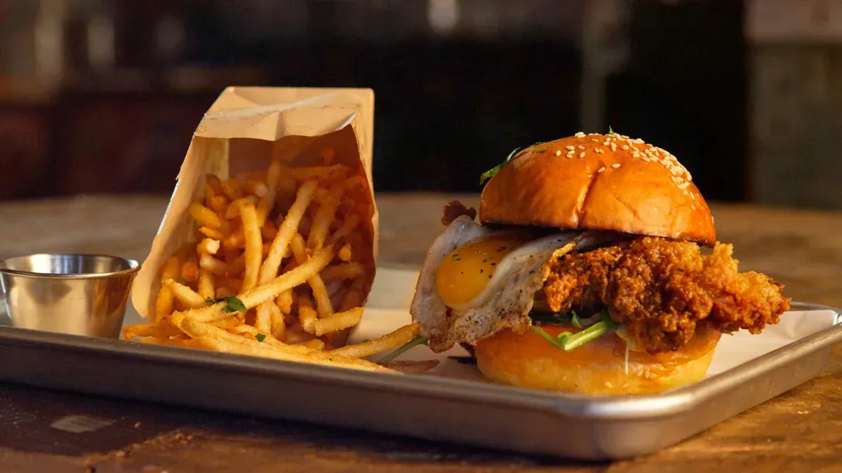 Tray with a burger, fries in a paper cup, and a small sauce cup on a restaurant table