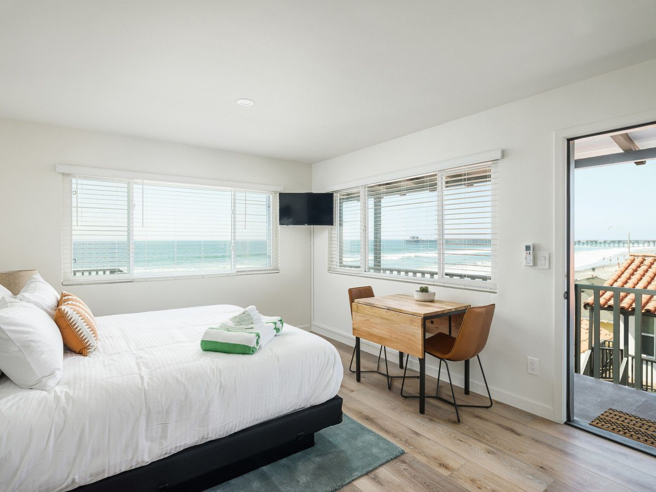 Bright bedroom with white bed, desk, windows, and ocean view through the open door