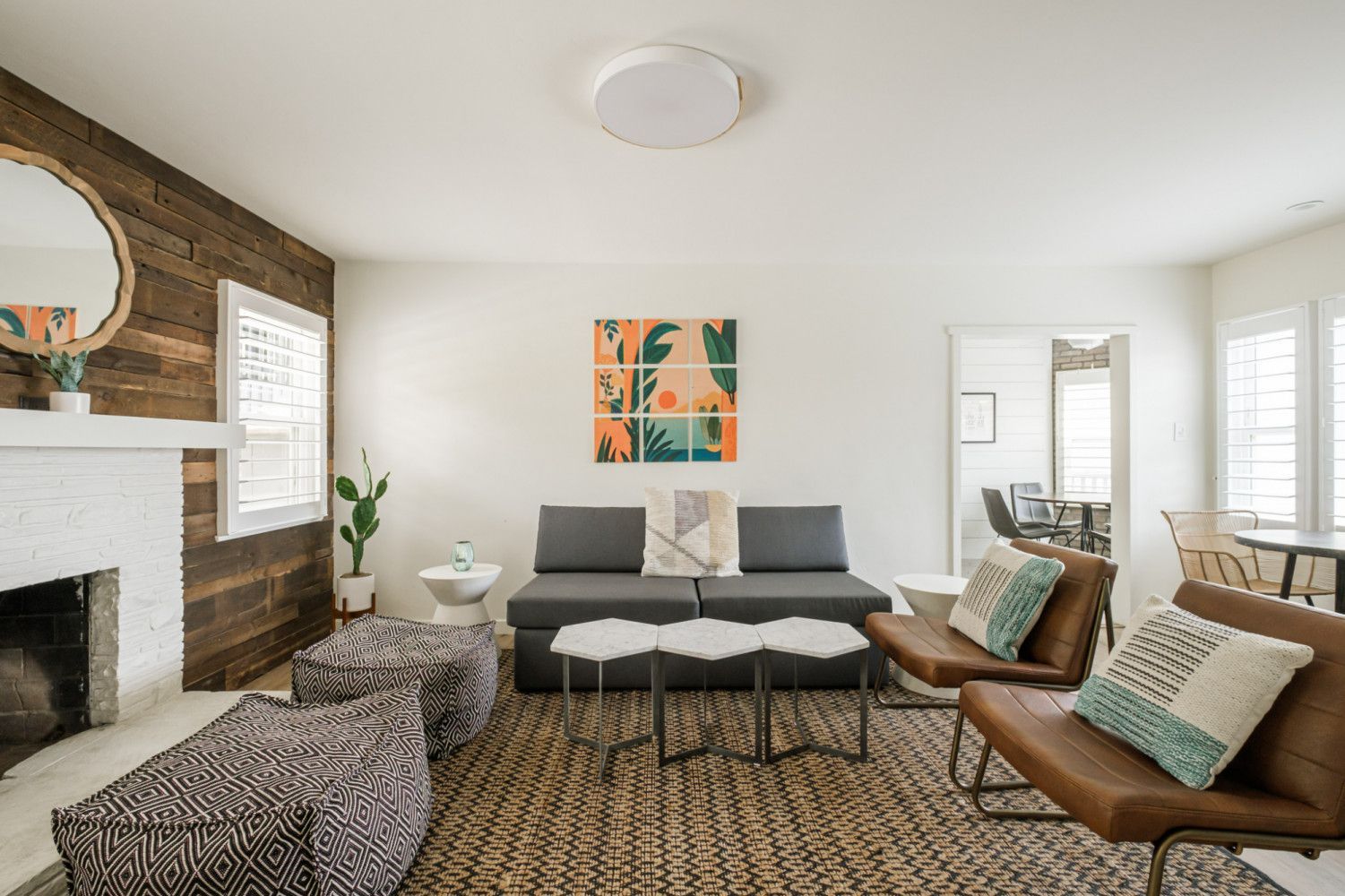 Bright living room with fireplace, gray sofa, brown chairs, patterned rug, and colorful wall art