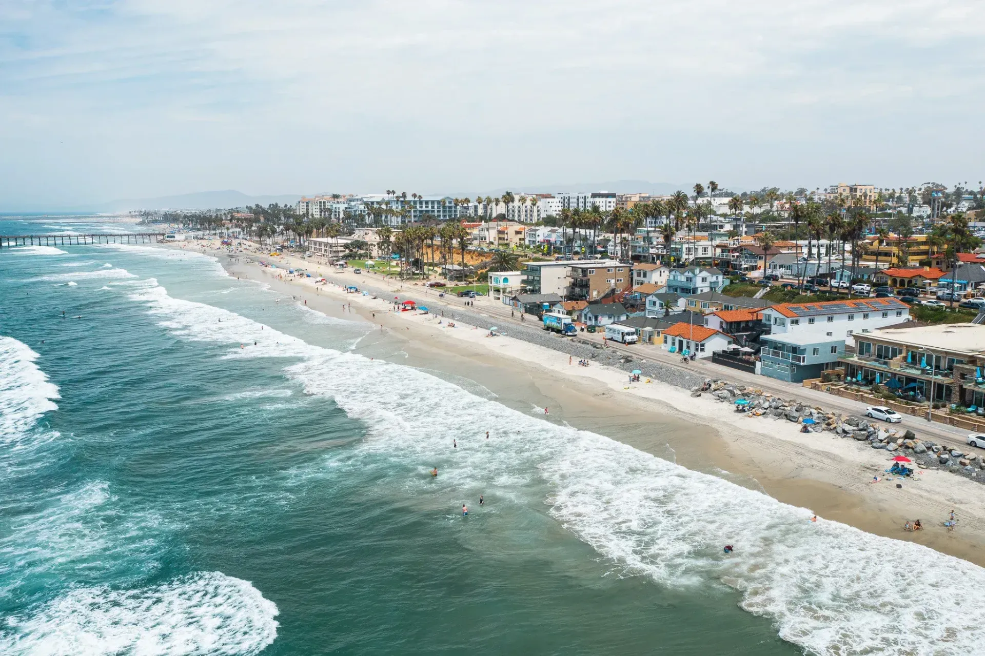 Aerial view of a sandy beach with ocean waves and a coastal town along the shoreline.