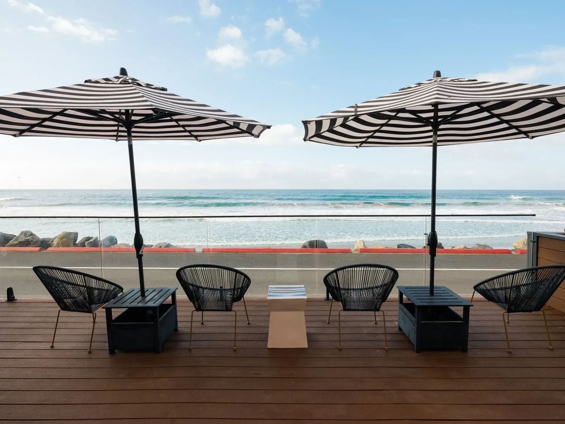 Beachfront patio with striped umbrellas, black chairs, and ocean view at sunset