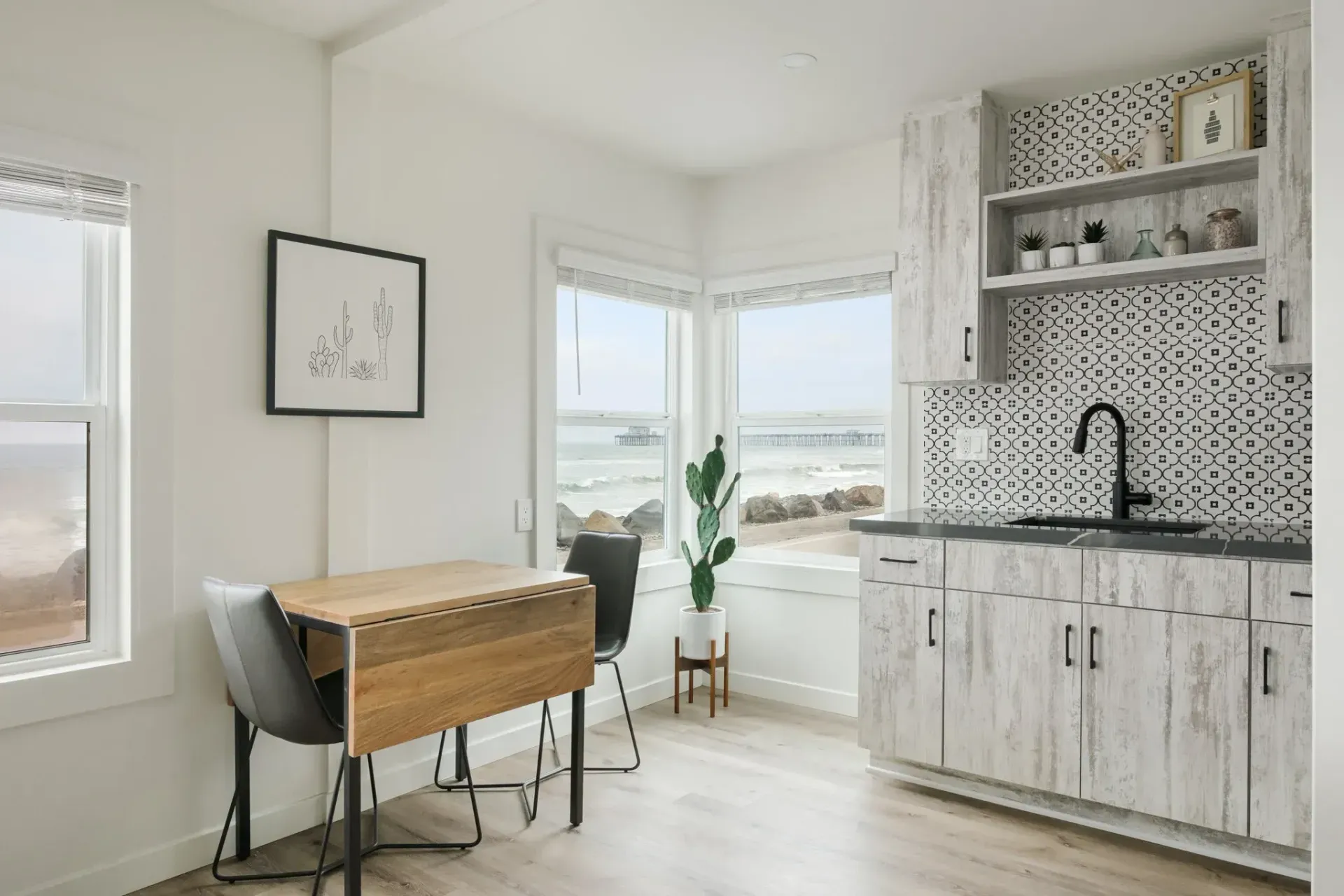 Bright kitchen with light wood cabinets, black faucet, mosaic backsplash, and a small table by the window.
