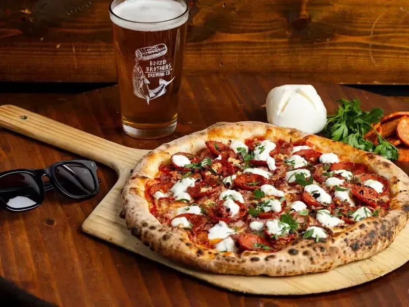 Pizza on a wooden board with sunglasses and a beer on a rustic table