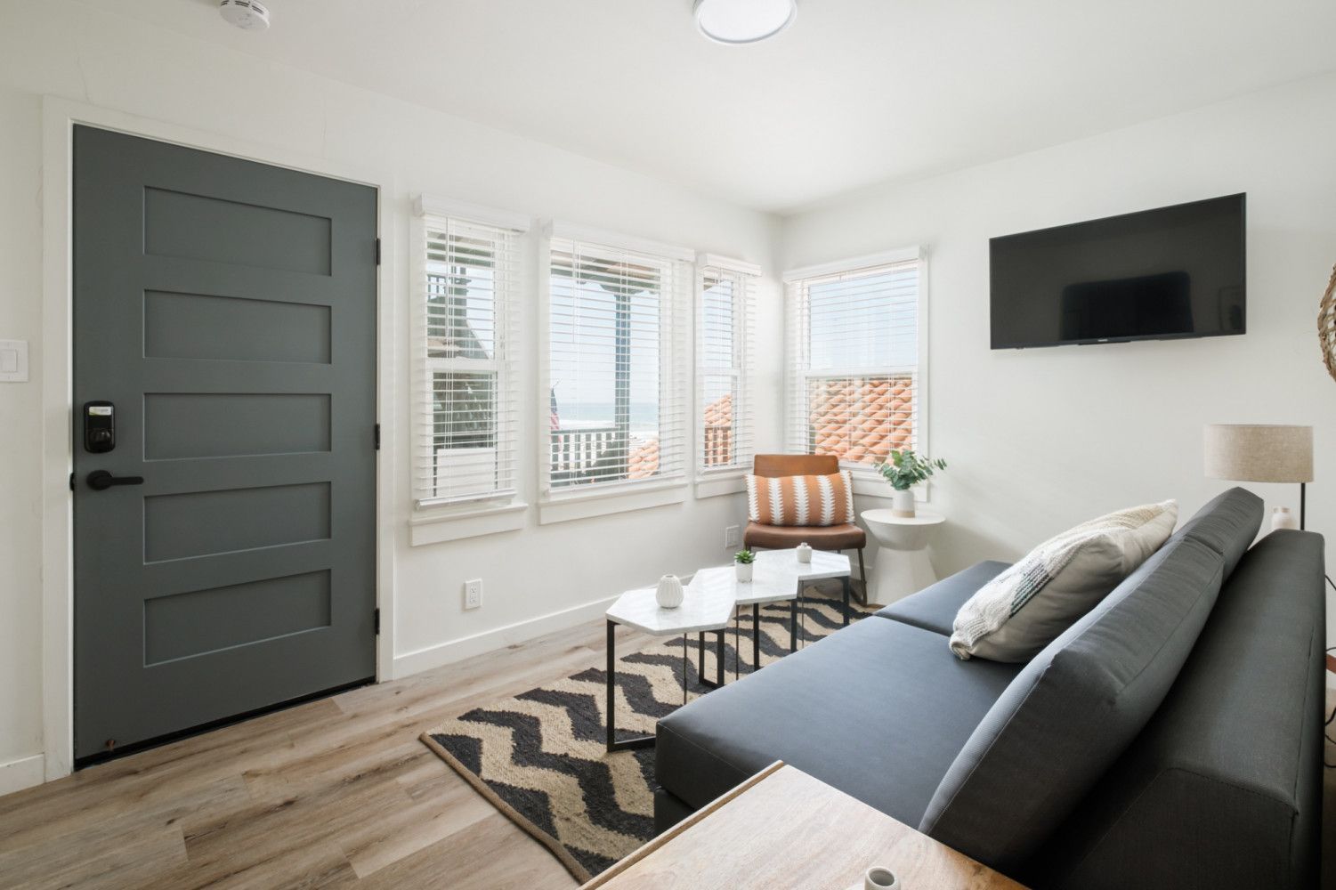 Bright living room with gray sofa, wall-mounted TV, windows, and modern geometric rug