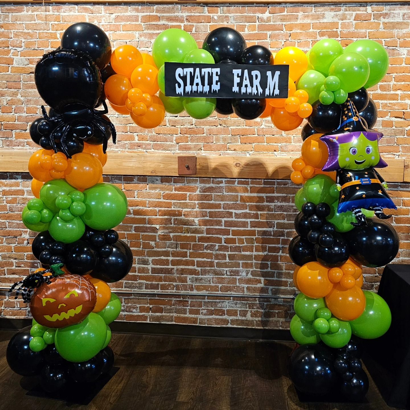 Halloween balloon arch with State Farm sign, black, orange, and green balloons, and jack-o’-lantern decorations