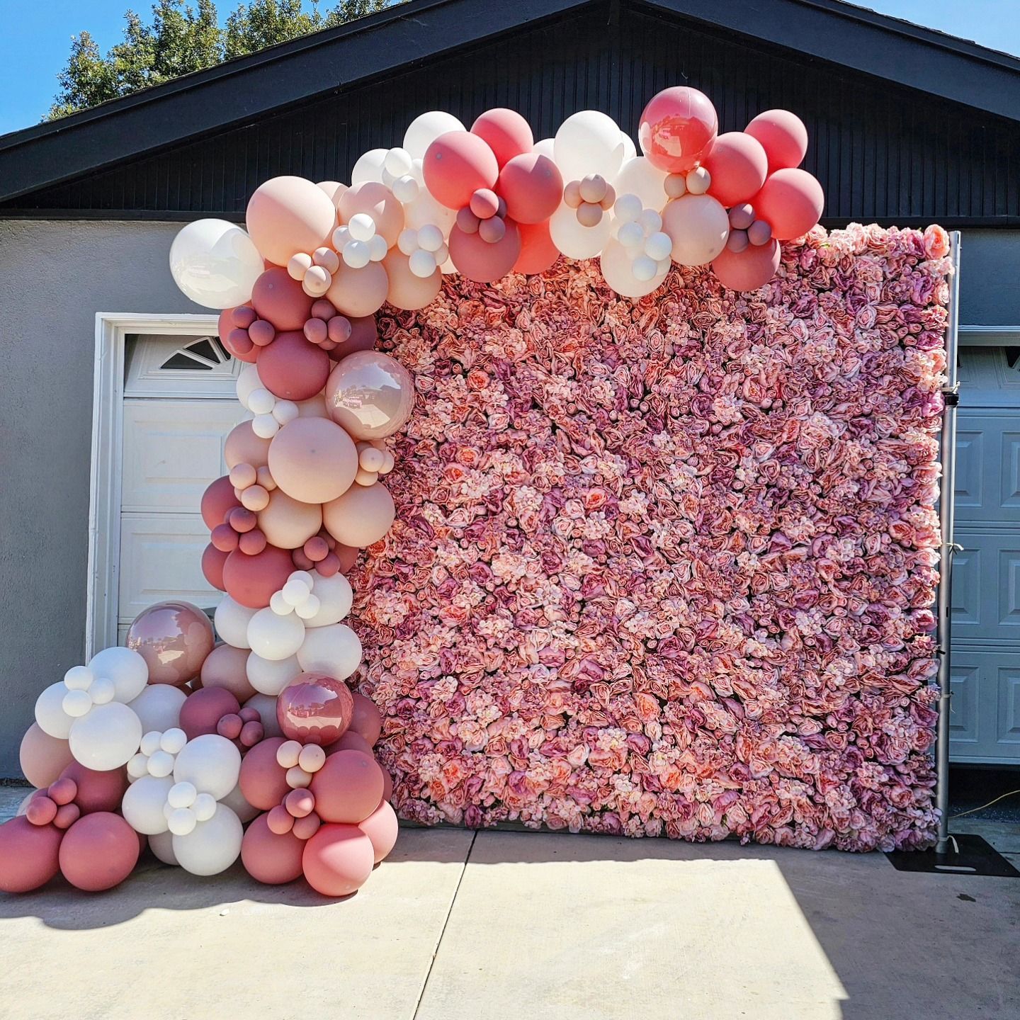 Balloon and flower photo backdrop beside a garage door on a driveway