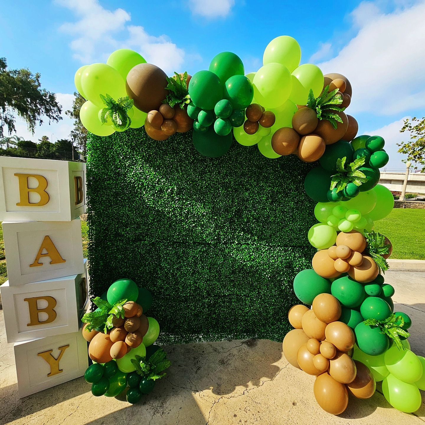Green balloon arch framing a hedge backdrop with stacked BAB blocks on the left and balloon clusters on the right