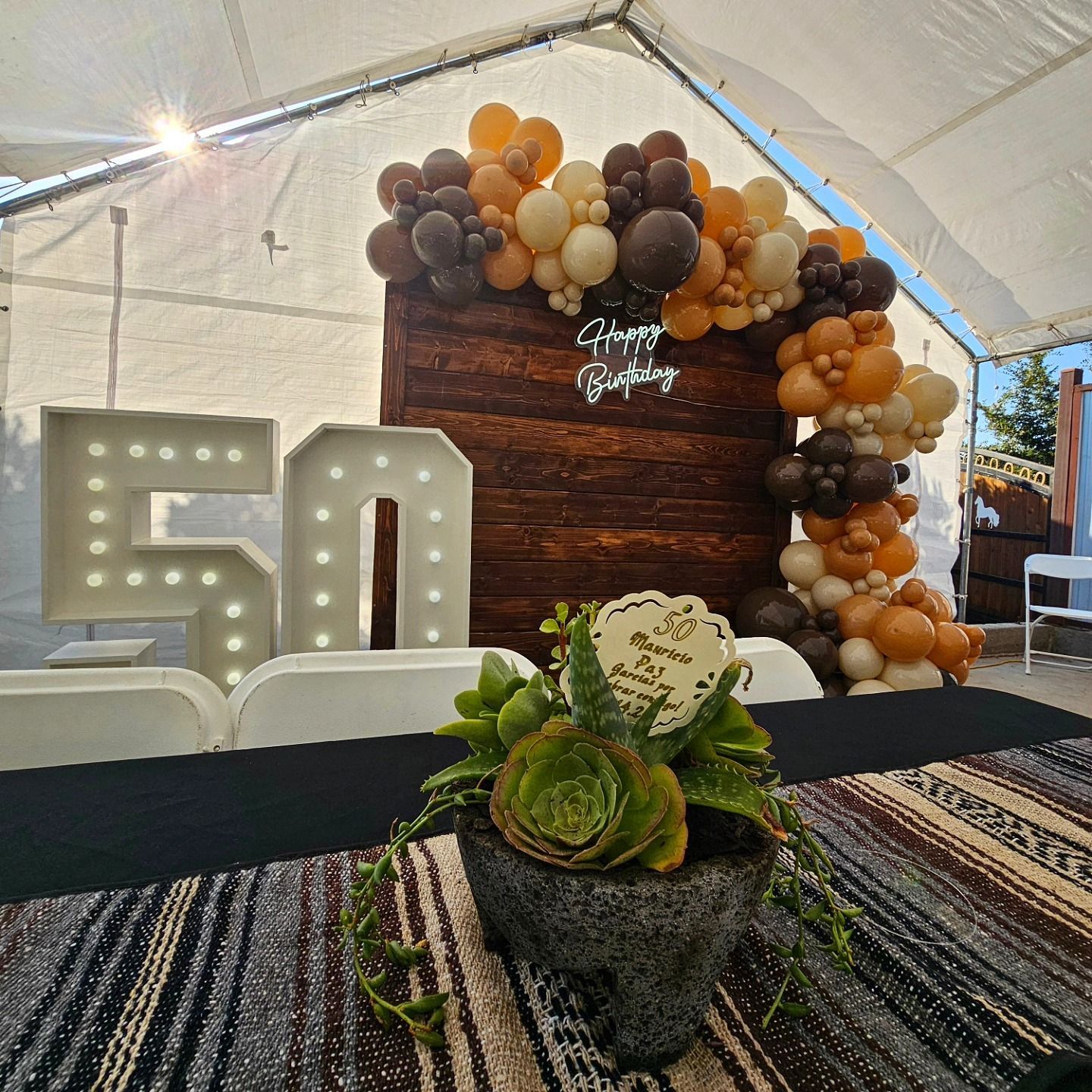 Birthday party display with large lit “50” numbers, balloons, and a flower centerpiece under a tent