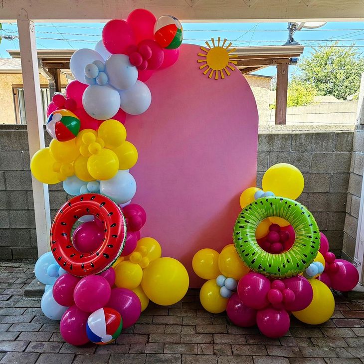 Colorful balloon backdrop with pink oval center, sun decoration, and bright balloon clusters on a patio
