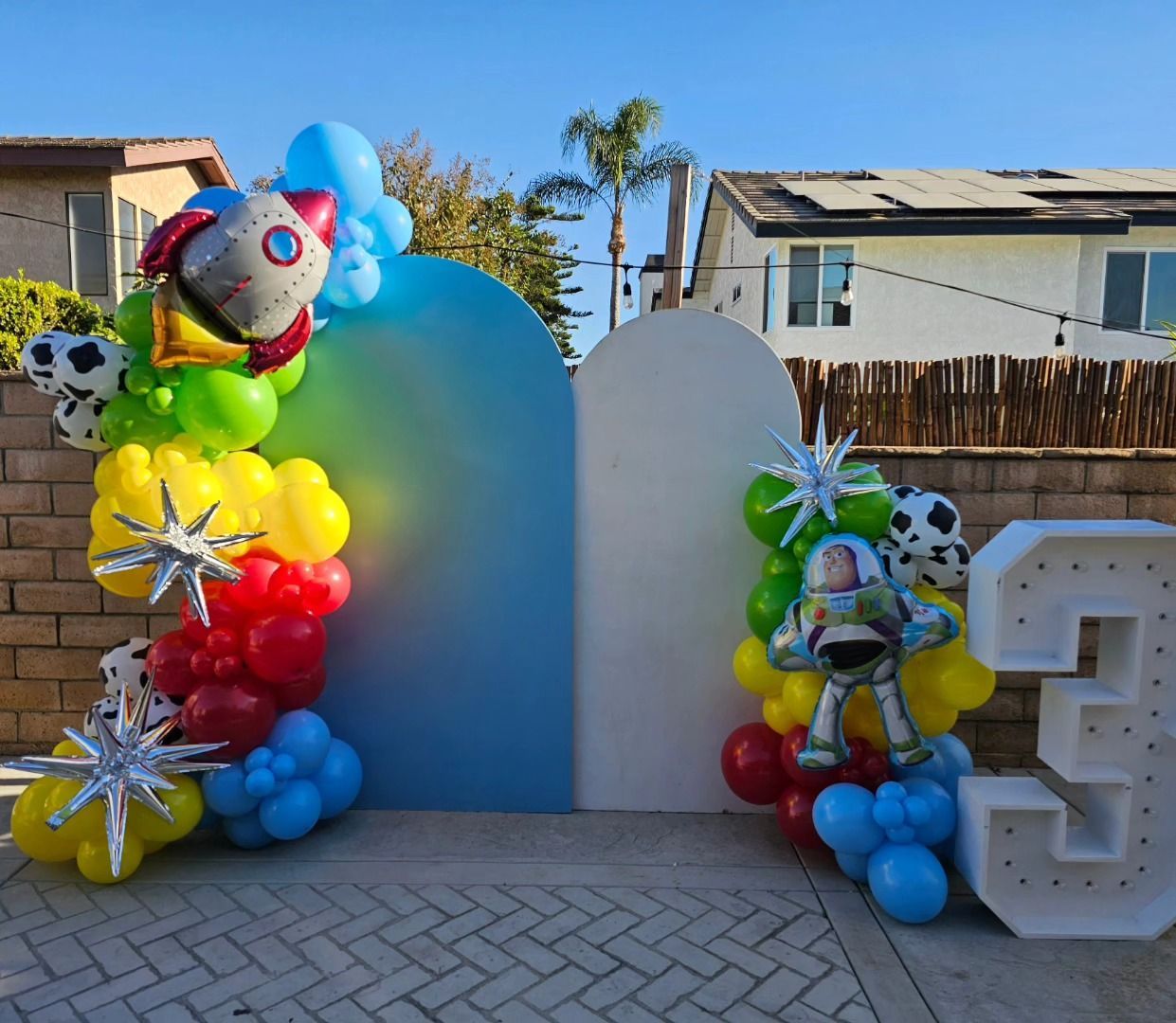 Colorful balloon birthday display with clown faces, blue arch, and large white number 3 outdoors
