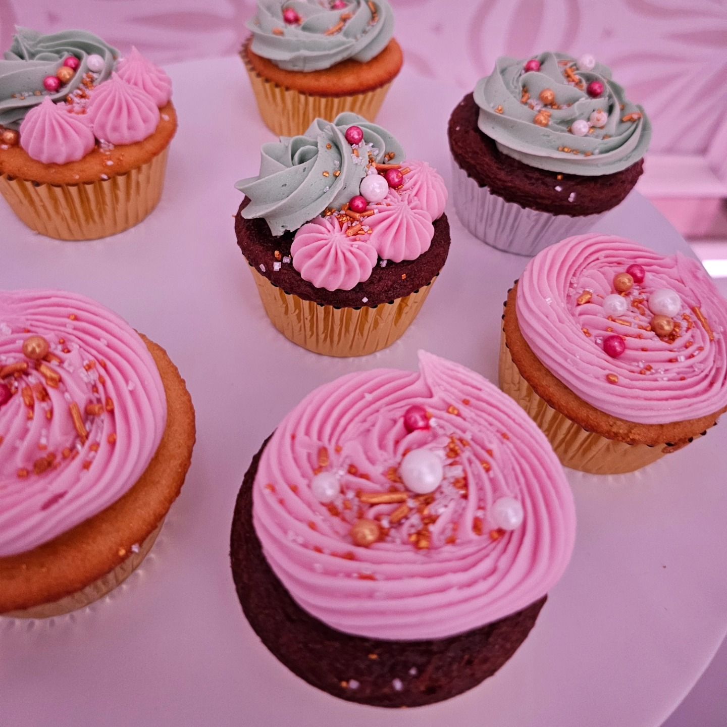 Pink-frosted cupcakes with sprinkles arranged on a pink tray