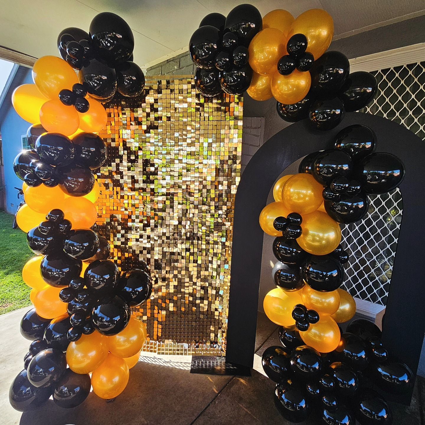 Black and orange balloon arch framing a gold sequin backdrop and a black archway entrance