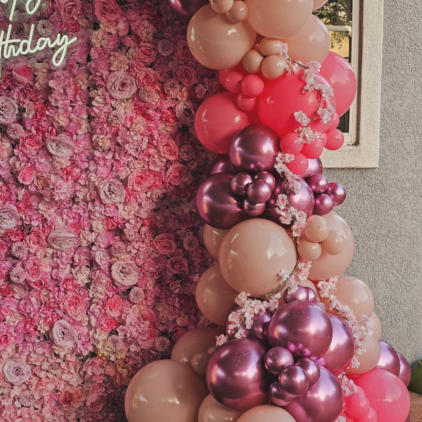 Pink floral backdrop with a balloon column in blush, rose gold, and magenta tones