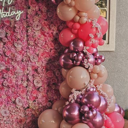 Pink and gold balloon arch beside a pink floral backdrop with a partial “Happy Birthday” sign