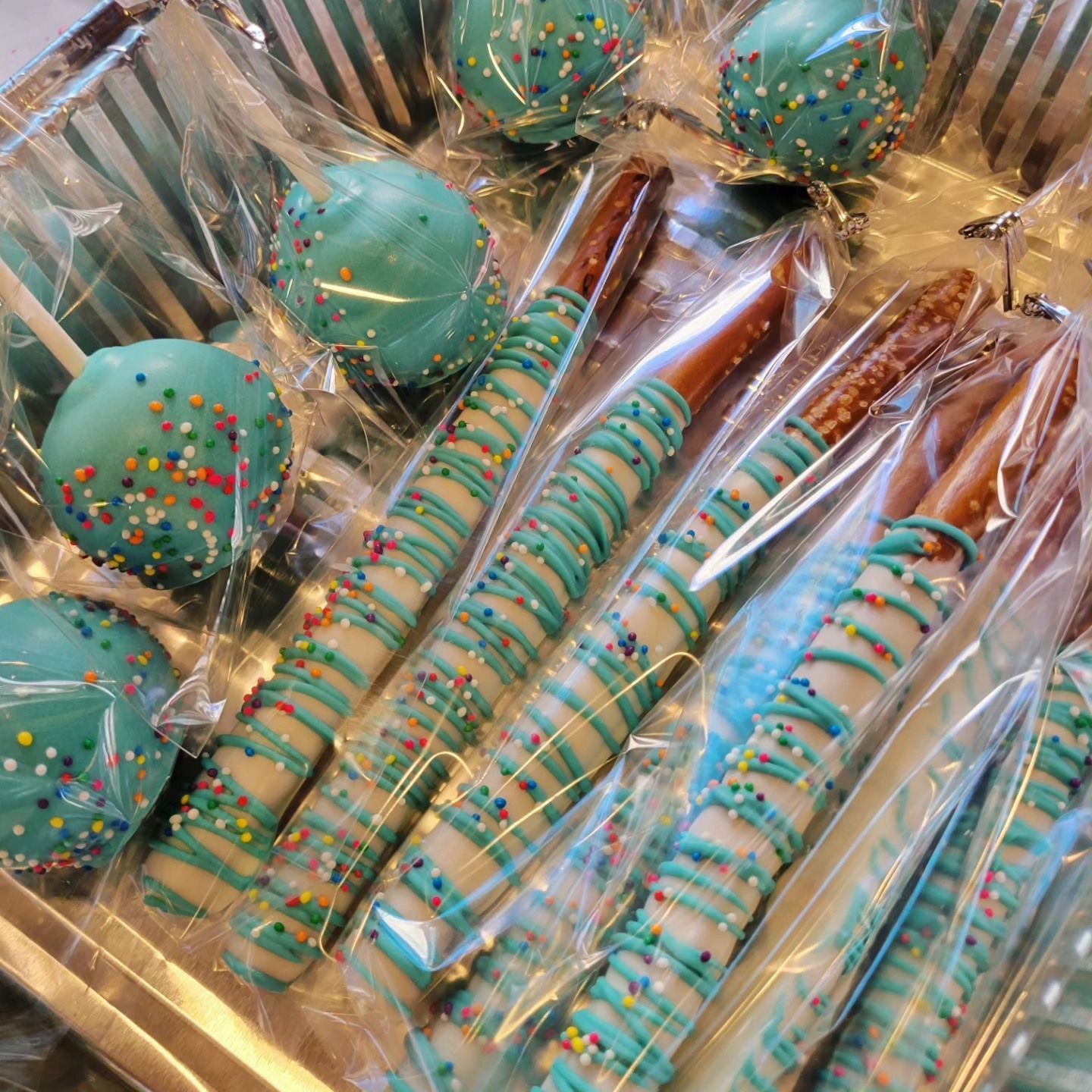 Turquoise and gold decorated cake pops and pretzel rods in clear wrapping