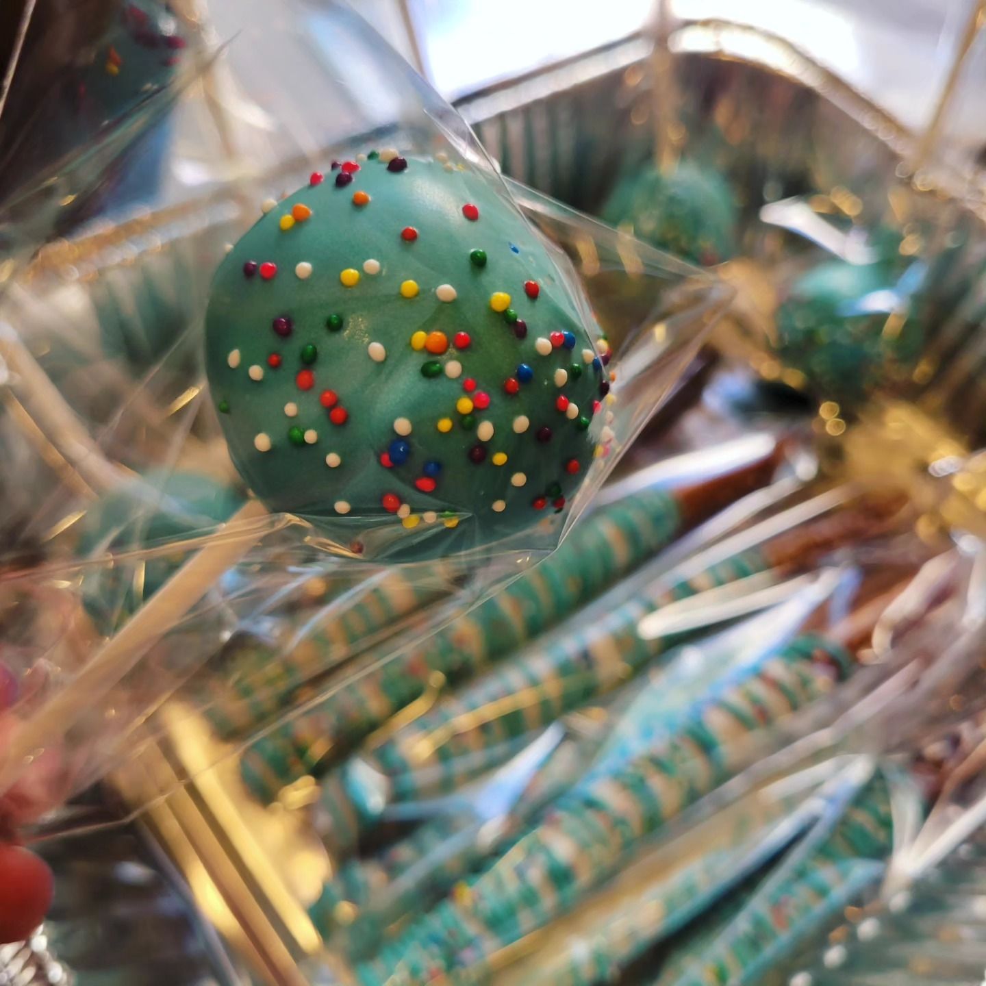 Green sprinkle-covered candy close-up among wrapped treats and gold ribbons