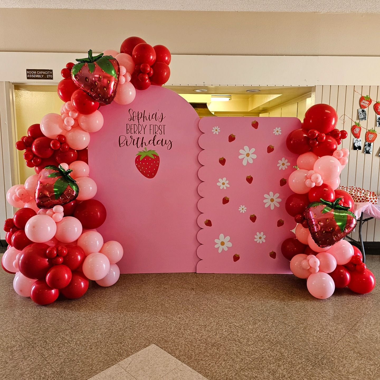 Pink Strawberry Shortcake birthday backdrop with red and pink balloon garlands and floral decorations
