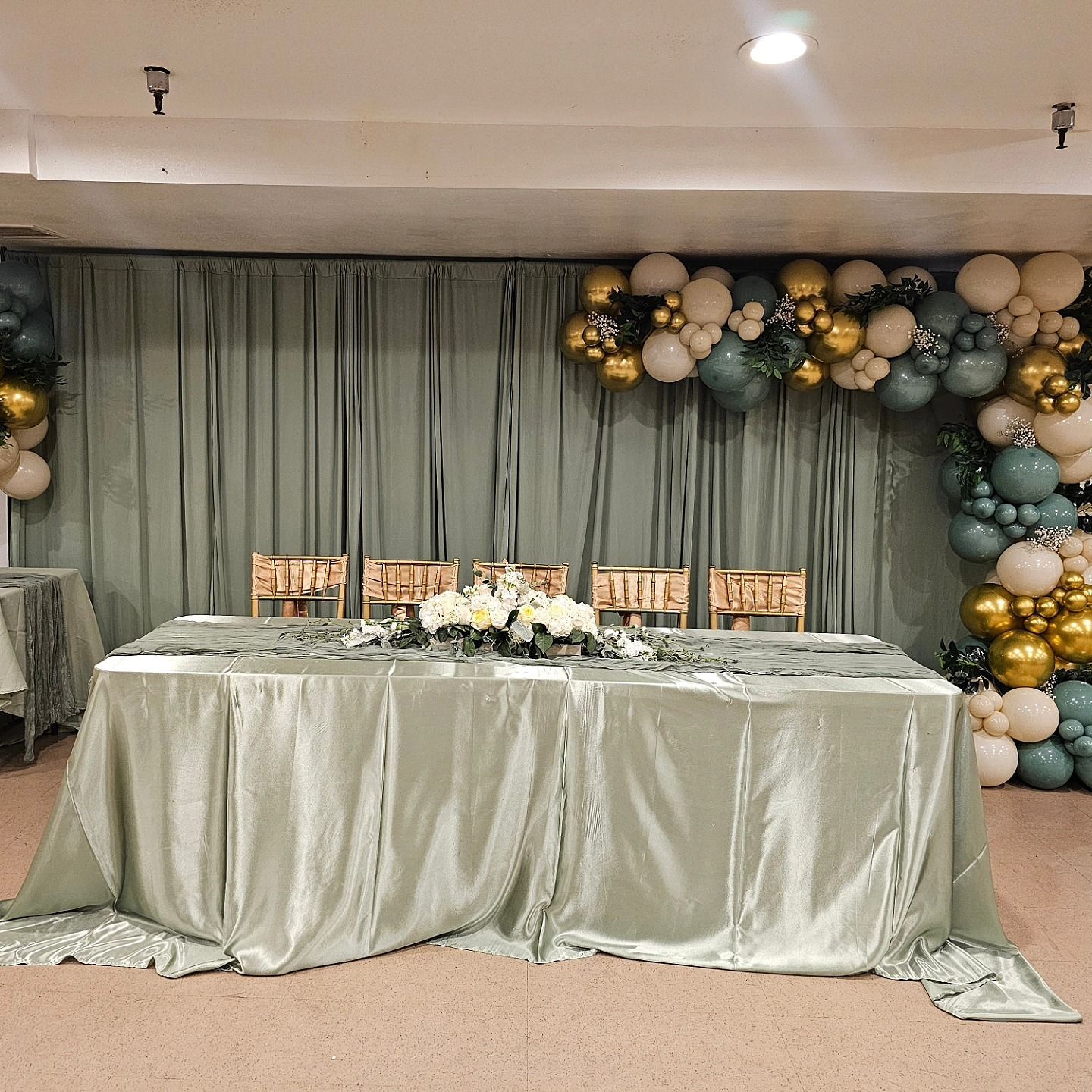 Decorated banquet table with silver drape and pastel balloon garland backdrop