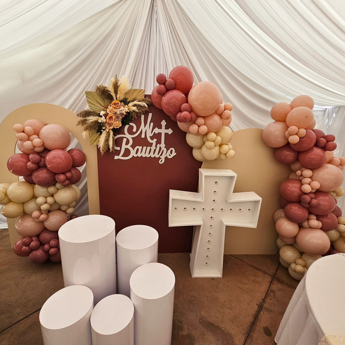 Pink and cream baby shower backdrop with balloon clusters, white cross, and “My Beauty” sign