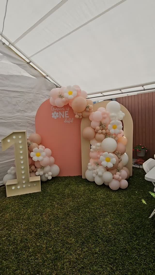 Pastel balloon arch and pink backdrop beside a gold number 1 at a party tent entrance
