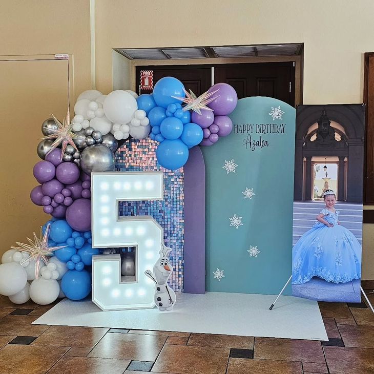 Blue and purple balloon display with a lit number 5, teal backdrop, and princess cutout at a birthday party