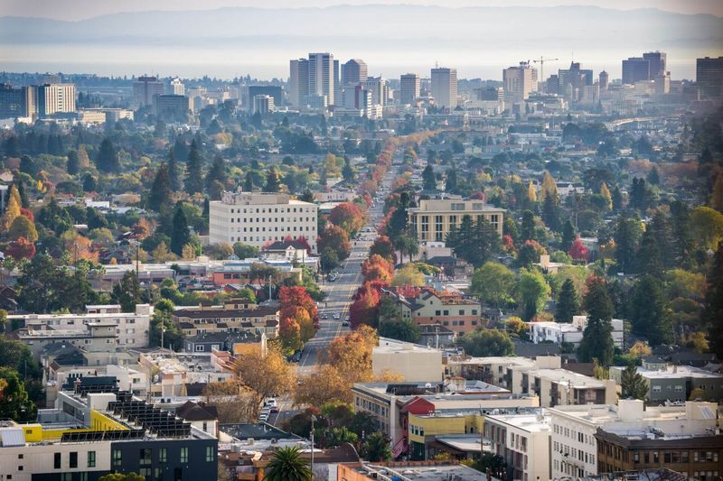 City skyline view, with tall buildings in the distance, a tree-lined street, and houses in the foreground.