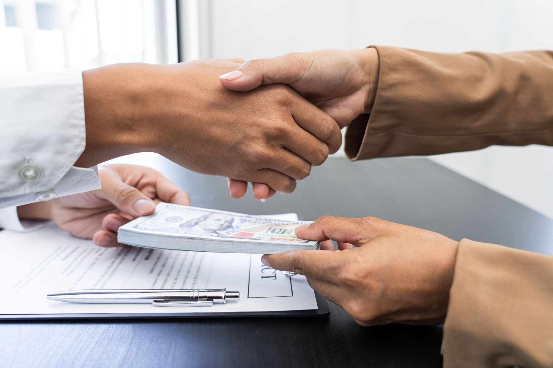 Person handing cash over a document, shaking hands.