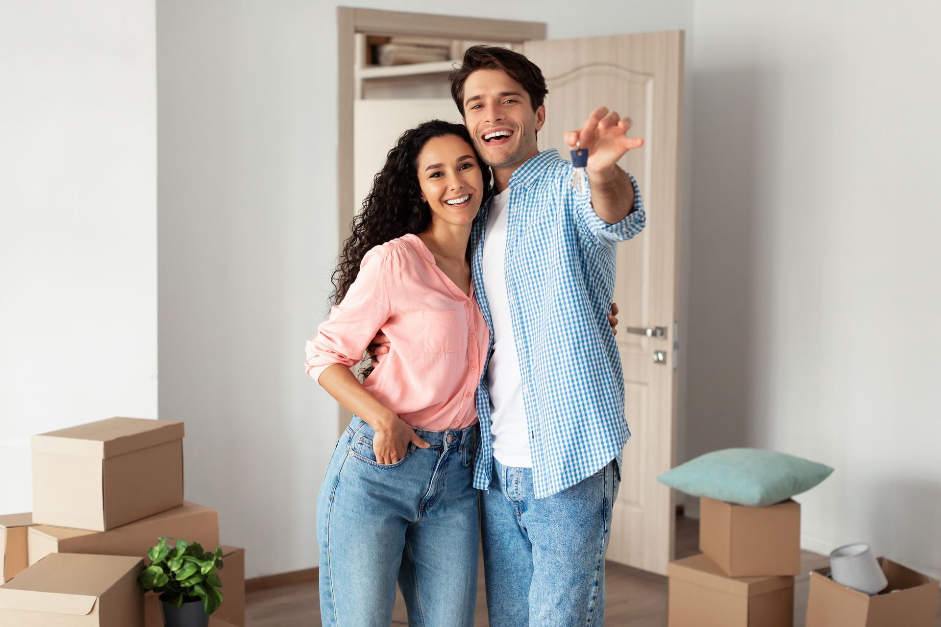 Couple holding keys, smiling, in new home with moving boxes.