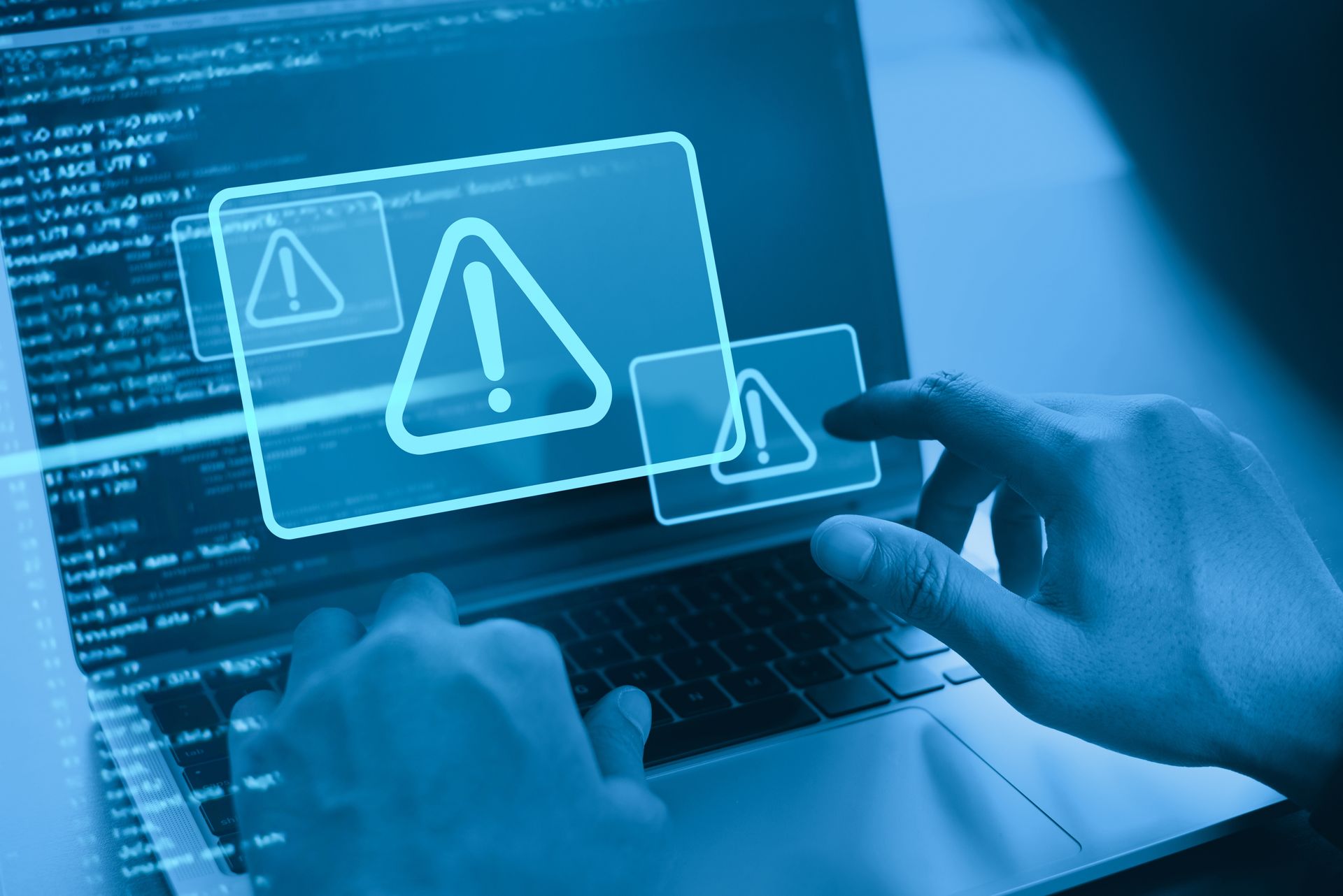 Hands interacting with a laptop displaying warning icons, blue-toned, hinting at a cyber security issue.