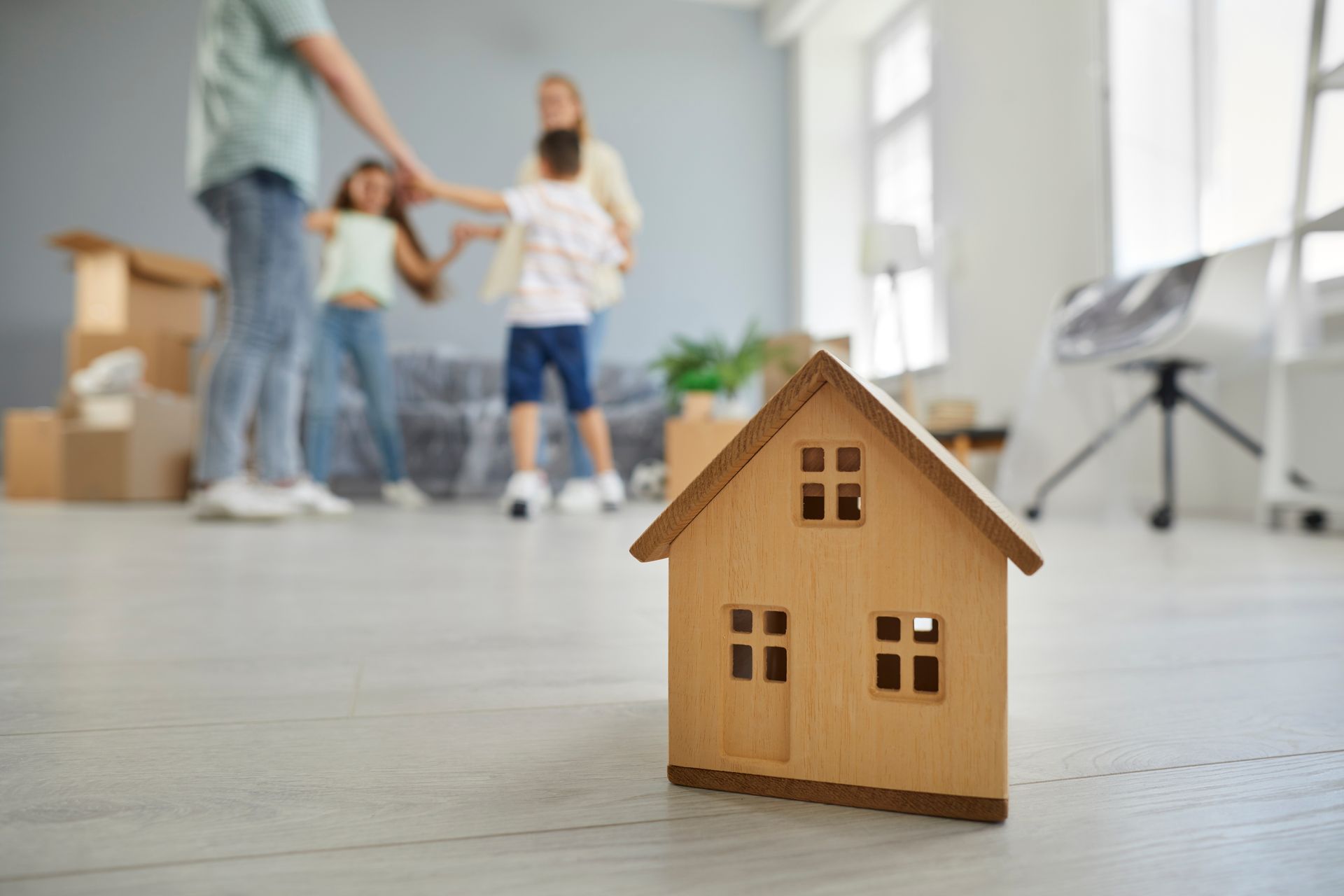 Wooden house model on floor, family in new home unpacking.