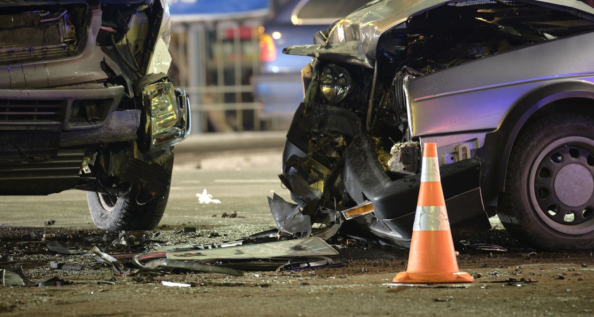 Two severely damaged cars on a street after a collision; orange traffic cone in foreground.