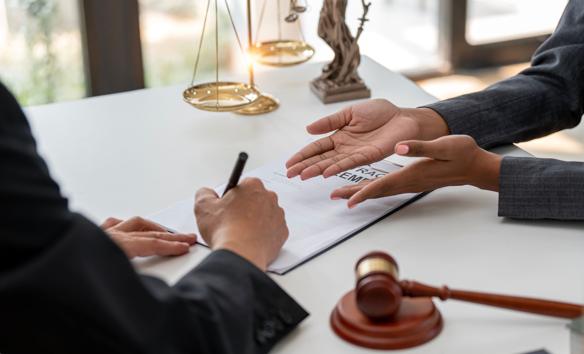 Hands pointing to a document as a person signs with a pen at a desk with a gavel and scales of justice in the background.