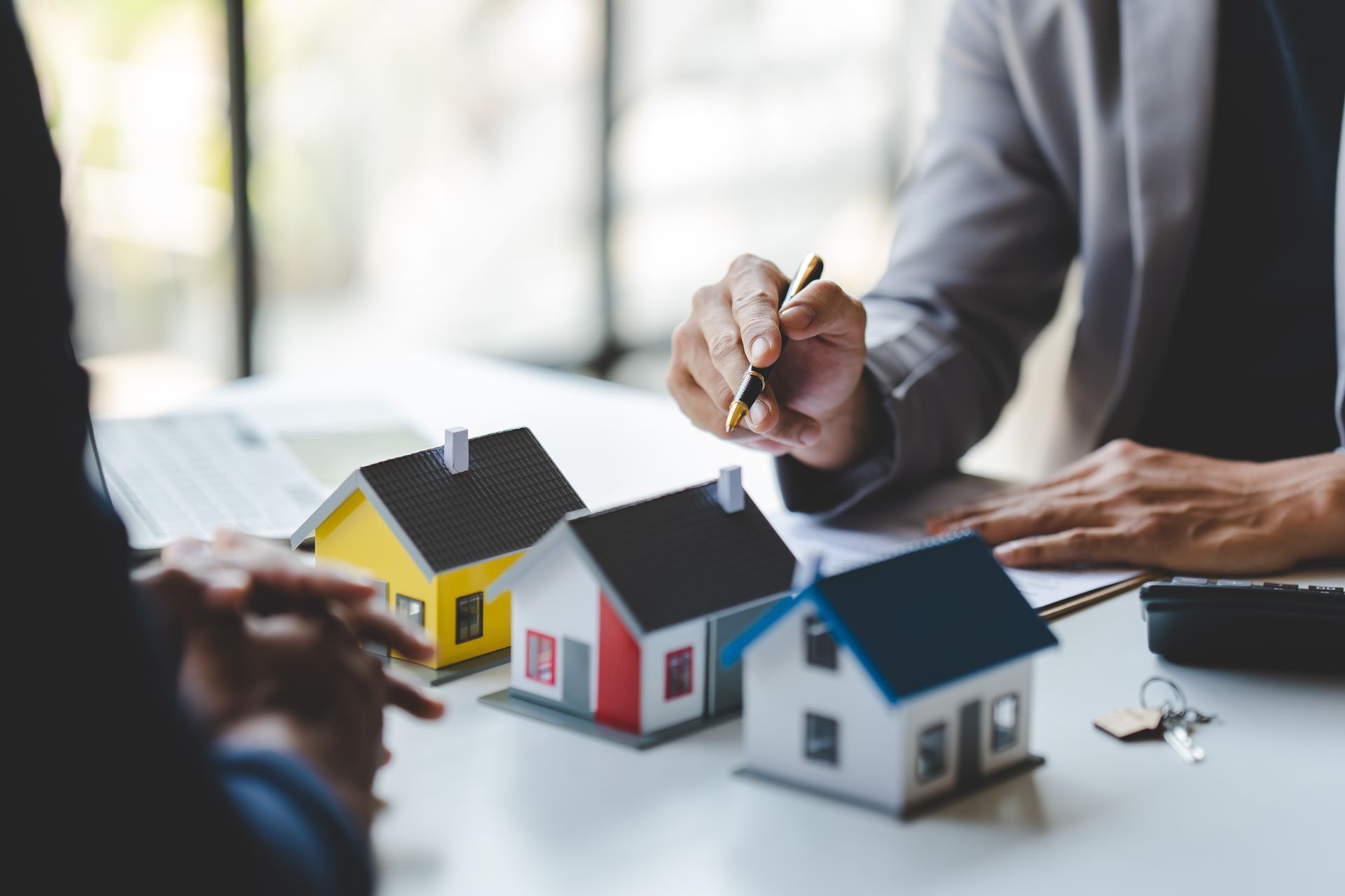 Real estate agents discussing miniature houses with a client, pointing to details on a table.