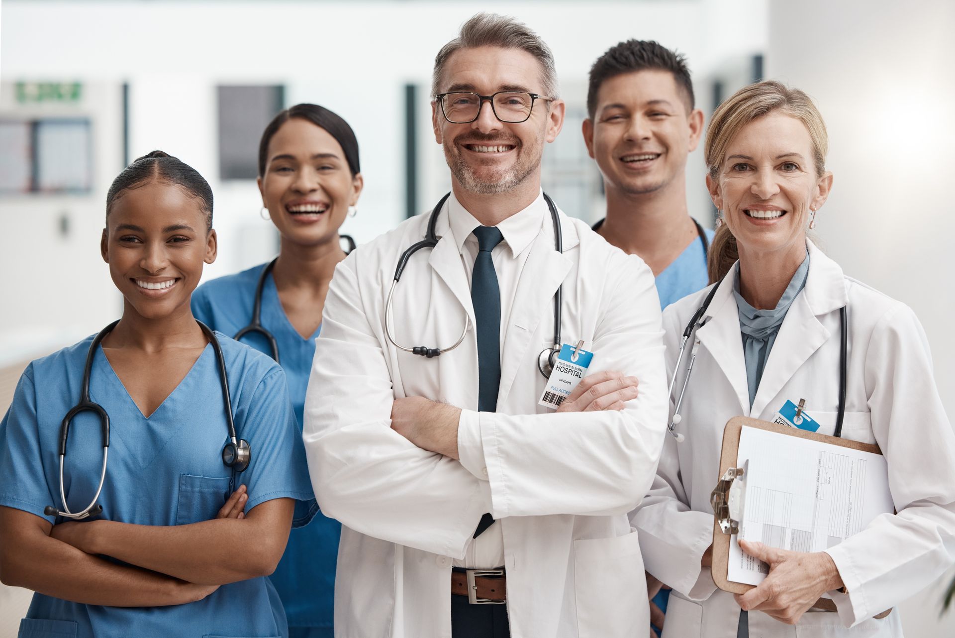 Medical team smiling, hallway setting. Doctors and nurses in scrubs and lab coats, stethoscopes.