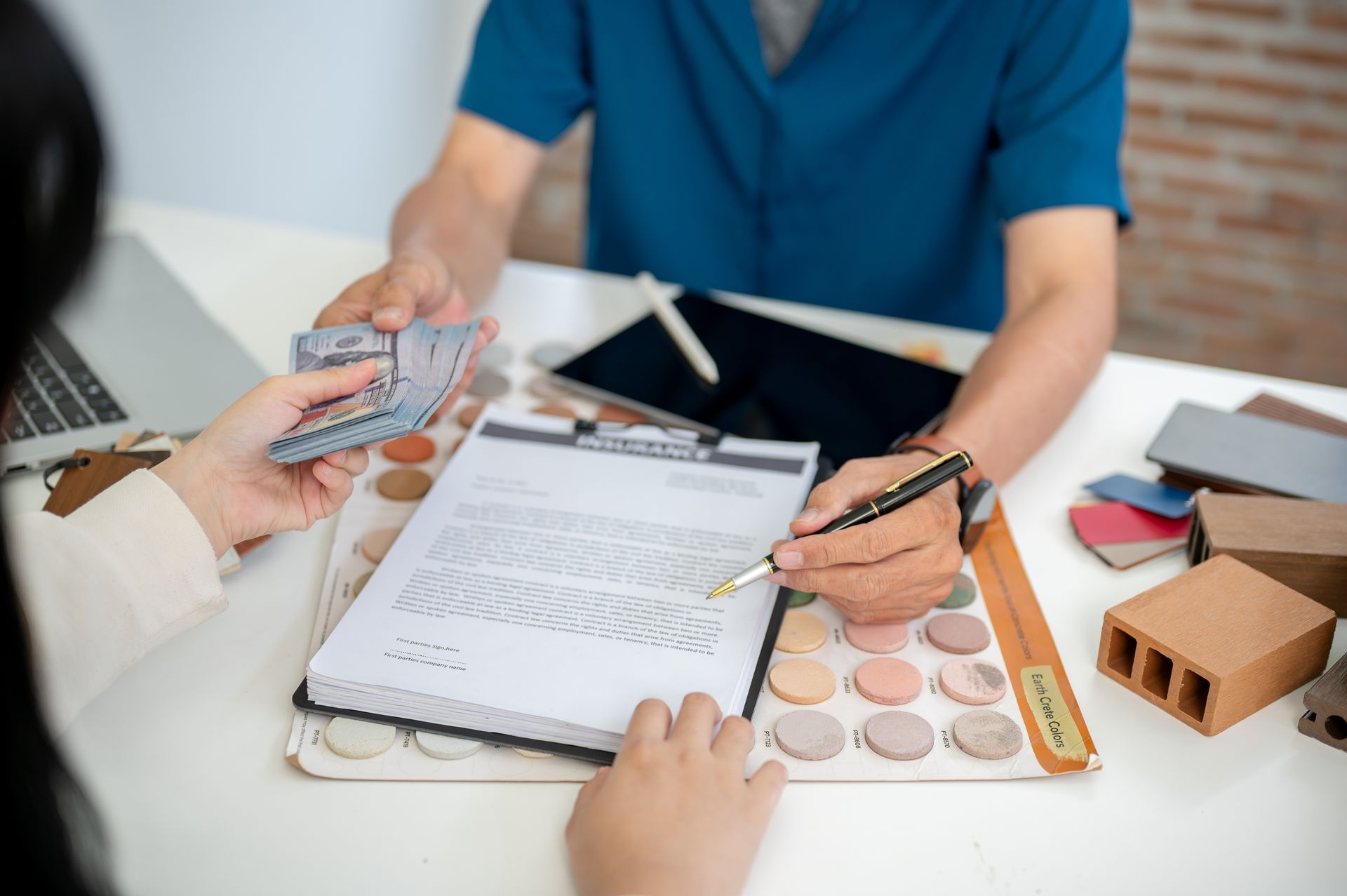 Person signing document, handing cash, near color swatches and samples on a table.