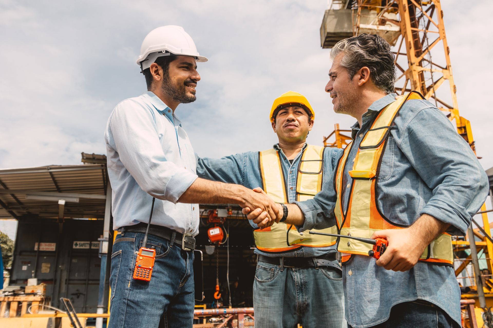 Construction workers shaking hands at a construction site; one in white hard hat smiles.