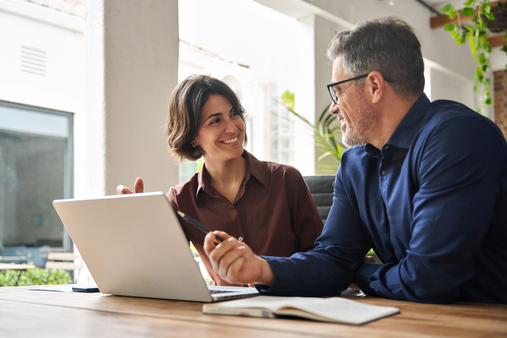Woman and man smiling at each other, looking at a laptop. They are in an office setting.