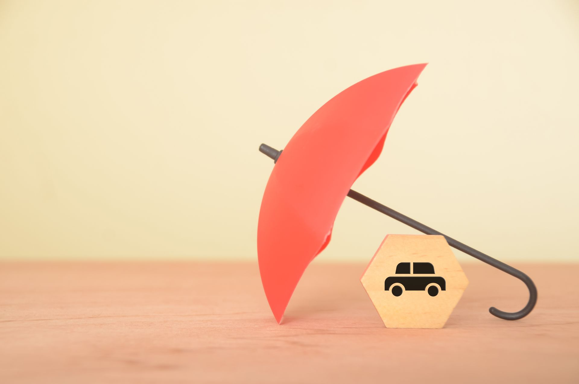 Red umbrella sheltering a wooden block with a car symbol, on a wooden surface.