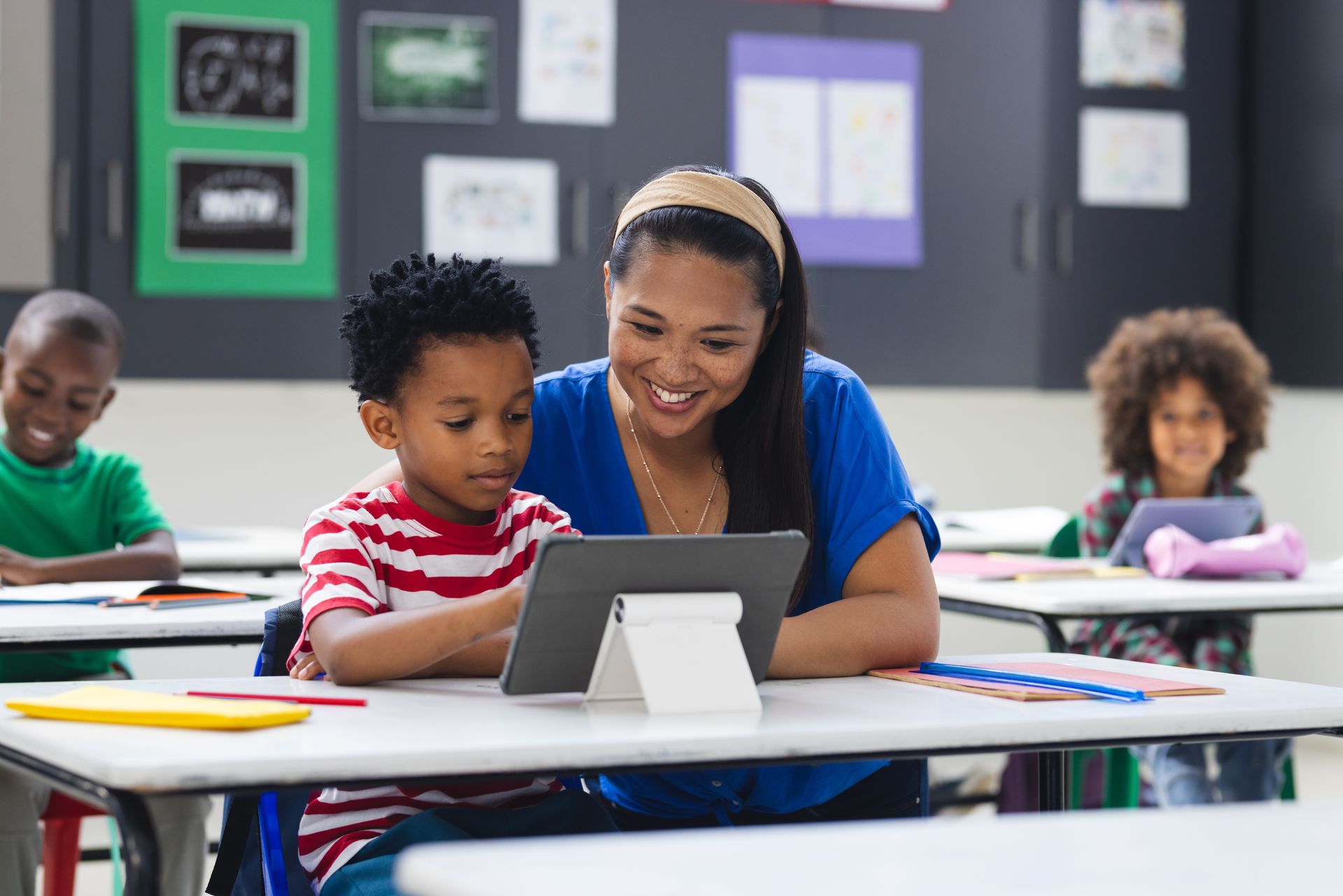 Teacher helping a child with a tablet in a classroom.