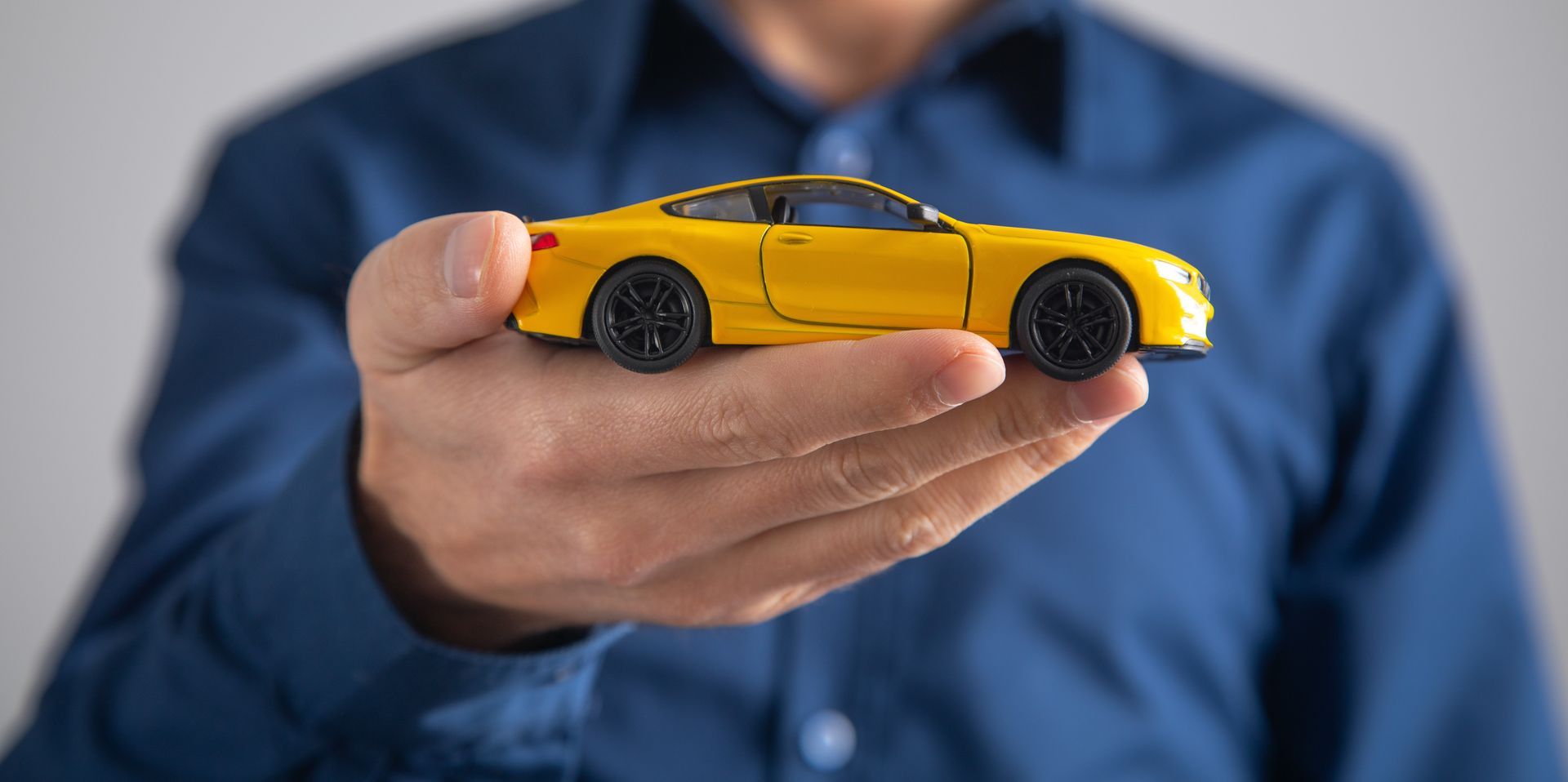 A person in a blue shirt holds a yellow toy car in their open palm.