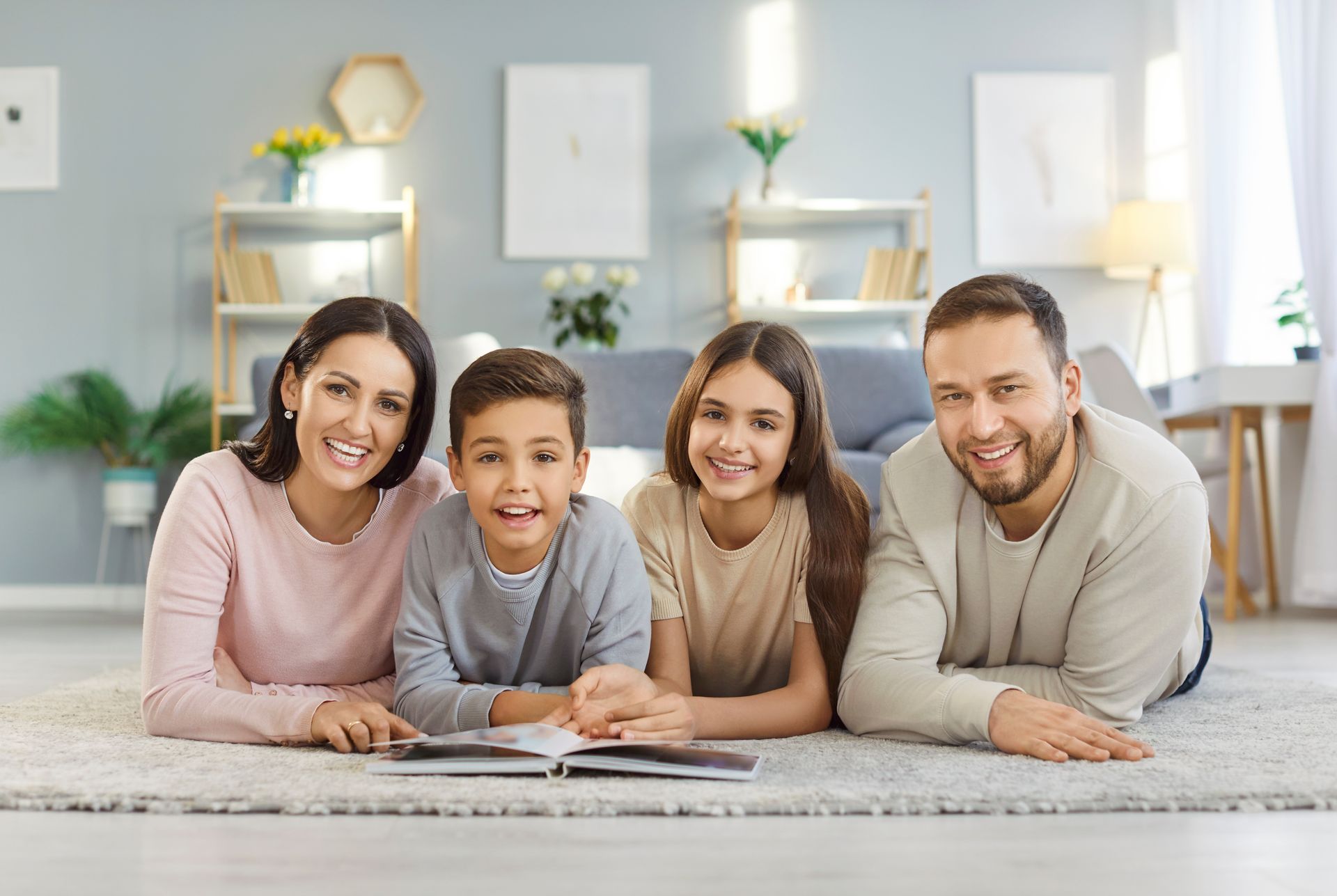 Family smiling and looking at a book on the floor in a living room.