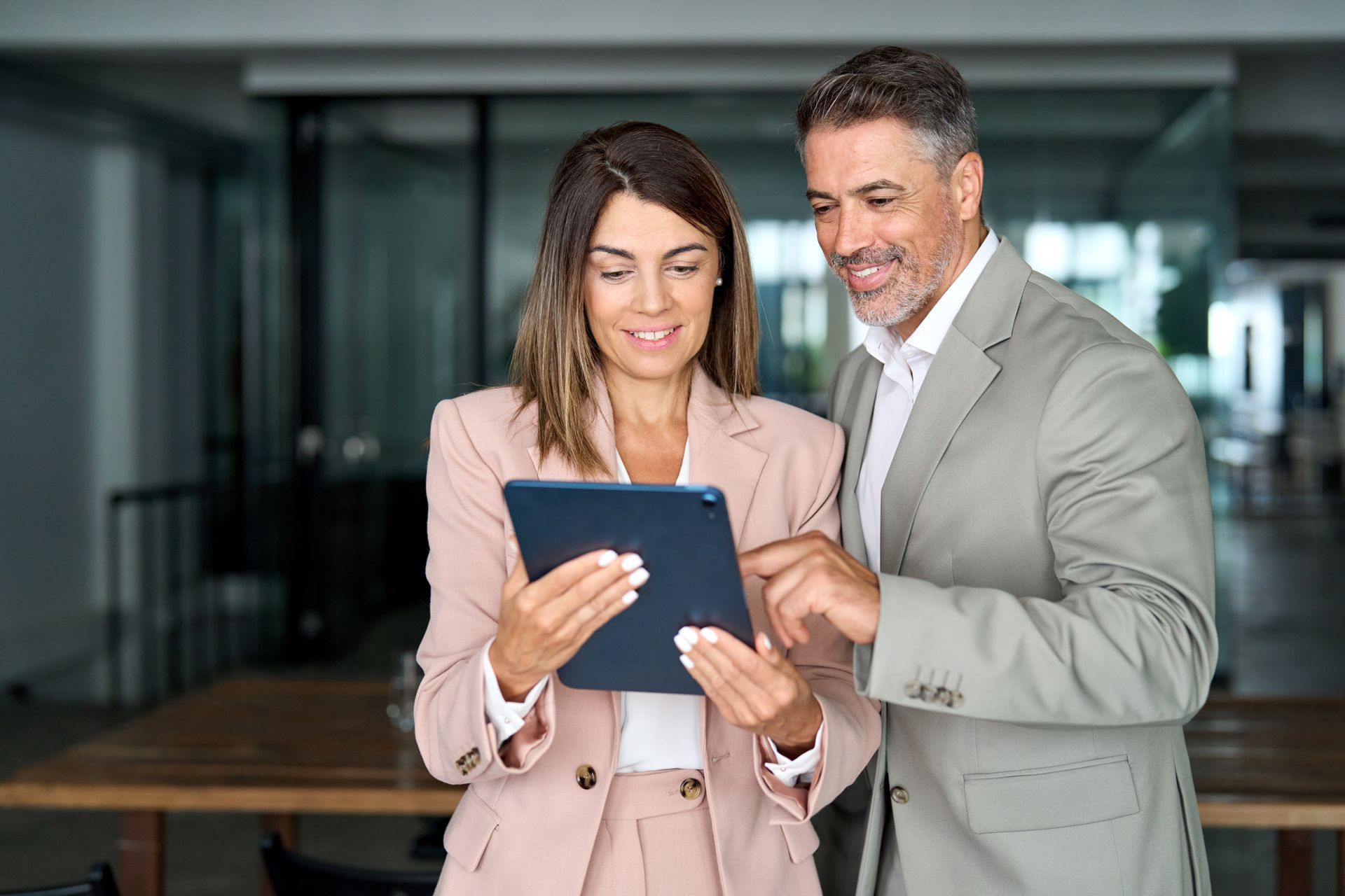 Woman and man in suits looking at a tablet together, smiling in an office.