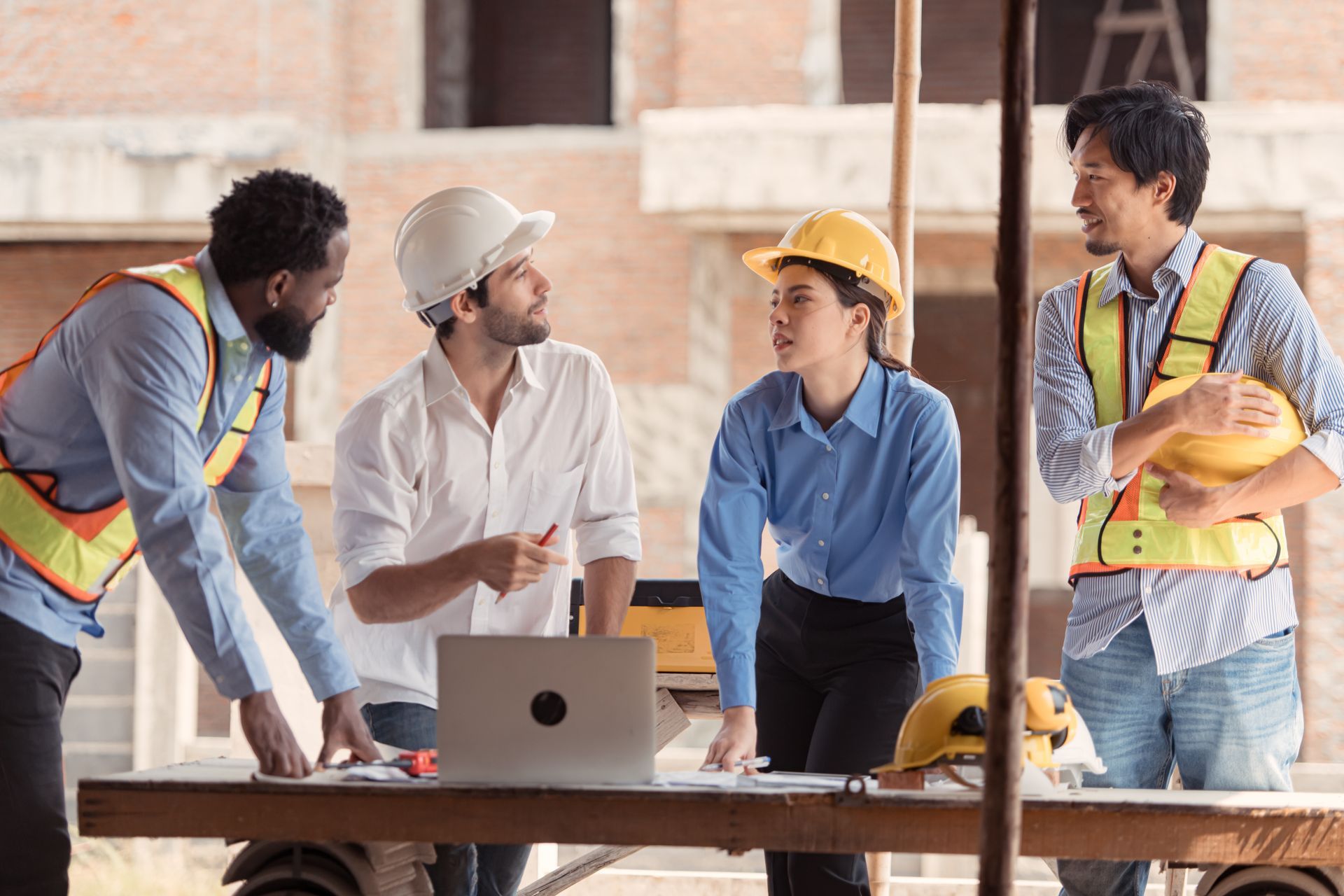 Construction workers in hard hats review plans at a table on a construction site.