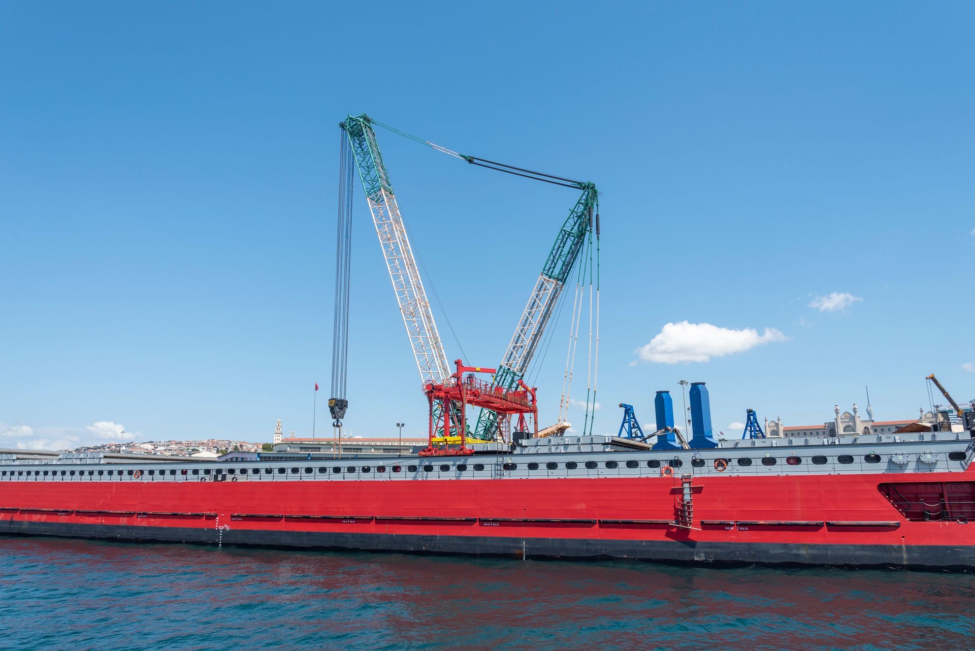 Large red crane on a barge in blue water, under a clear sky.